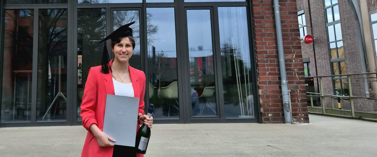 Rebecca Galkus mit ihrer Masterurkunde und Absolventenhut