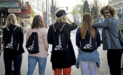 Junge Menschen laufen über die Straße, einer dreht sich um und lacht in die Kamera.