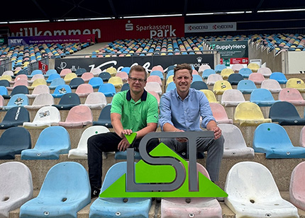 Julien Keibel (DHB) und Benjamin Willems (IST-Hochschule) sitzen im Stadion vor dem IST-Logo