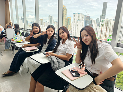 Vier thailändische Studentinnen sitzen nebeneinander und formen mit ihren Händen das Victory-Zeichen