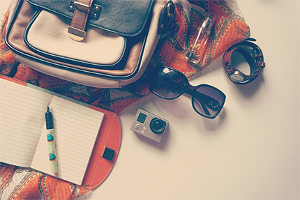 Geöffneter Rucksack, Sonnenbrille, Notizubuch auf Tisch